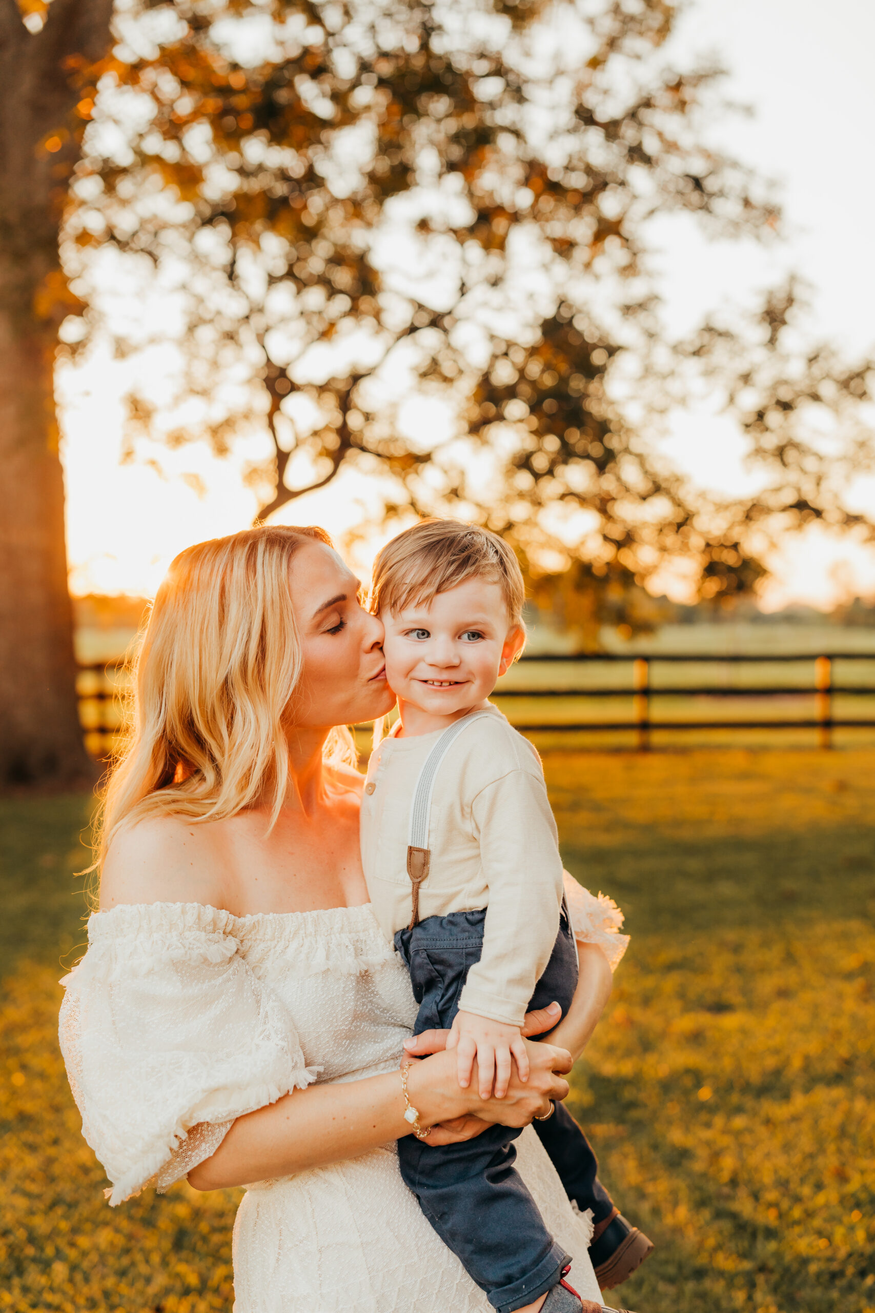 Mom kisses on son during a candid family photo session with Allyson Blankenburg, while standing under the families pecan trees on their farm during golden hour.