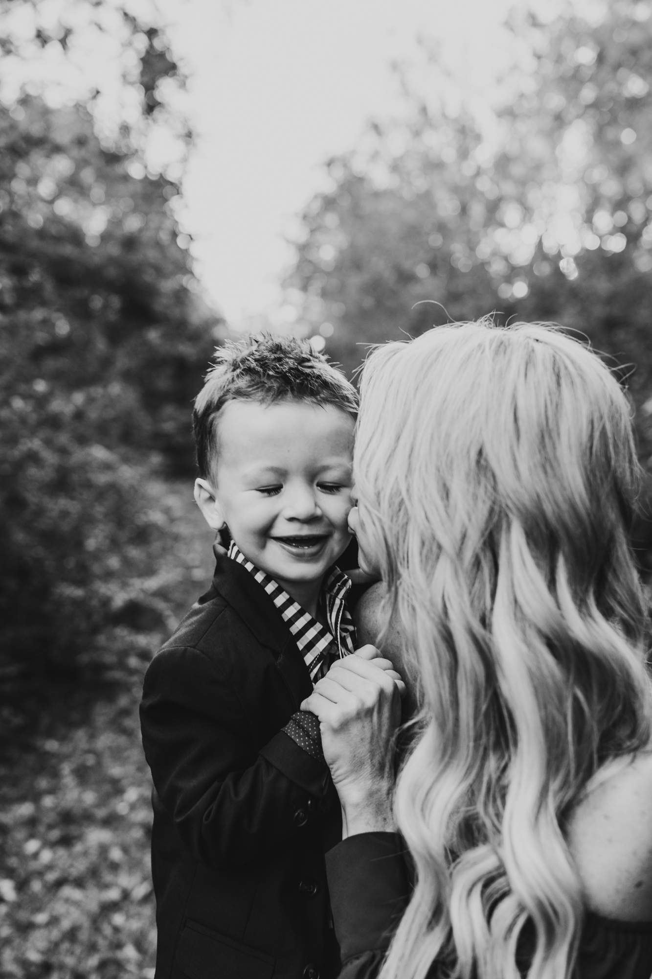 little boy get kiss on cheek from his mama in this black and white image, taken by Allyson Blankenburg