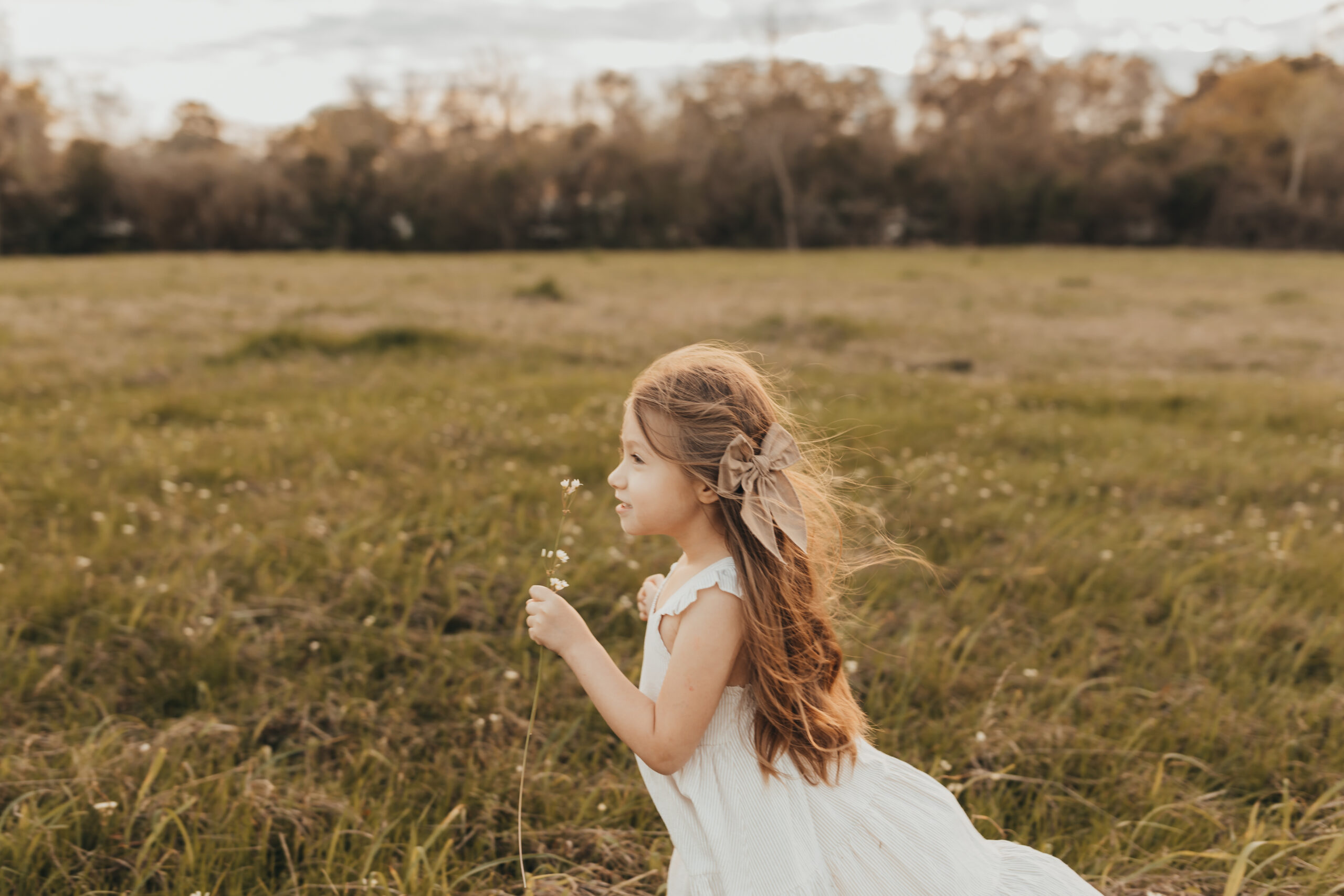 Little girl in field, smelling flowers, wearing clothing purchased from Houston Baby stores.