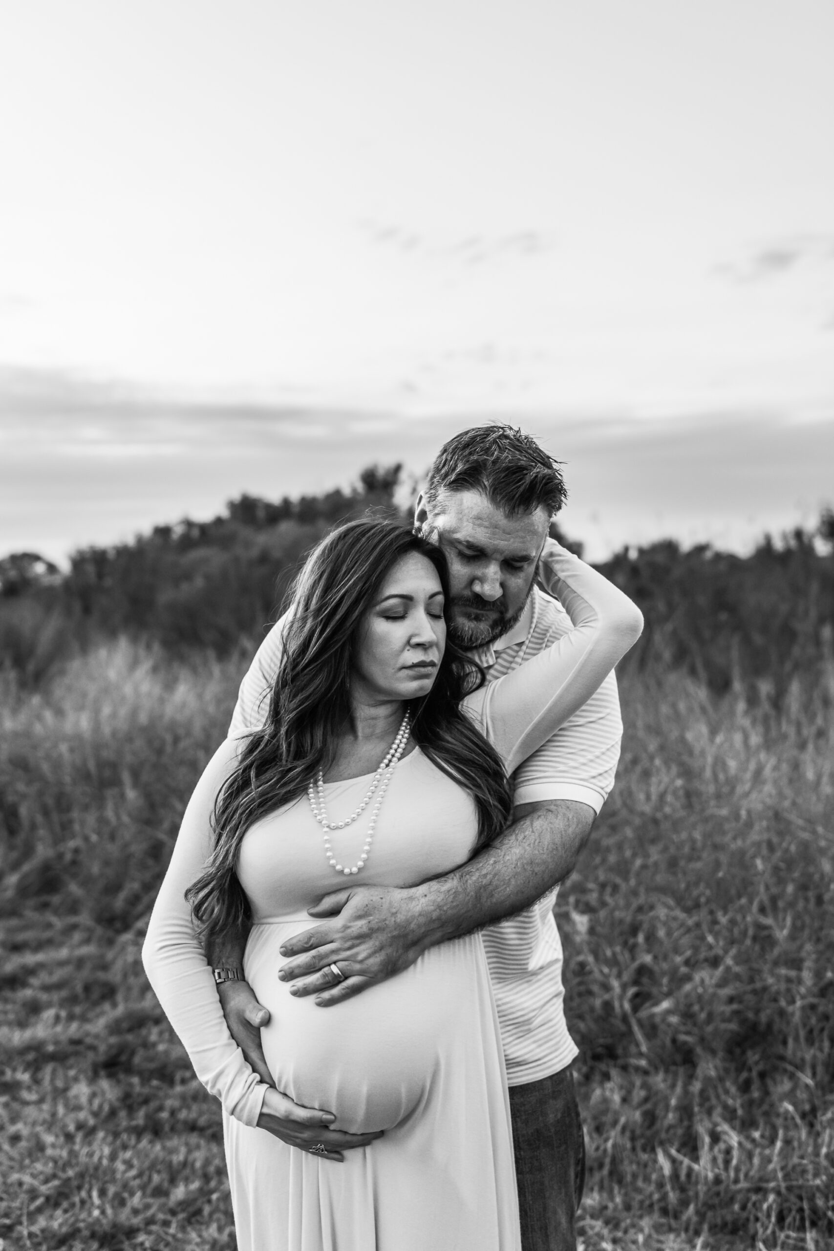 Allys photography capturing mom to be with her husband, dreaming about their growing baby while embracing each other in a field.