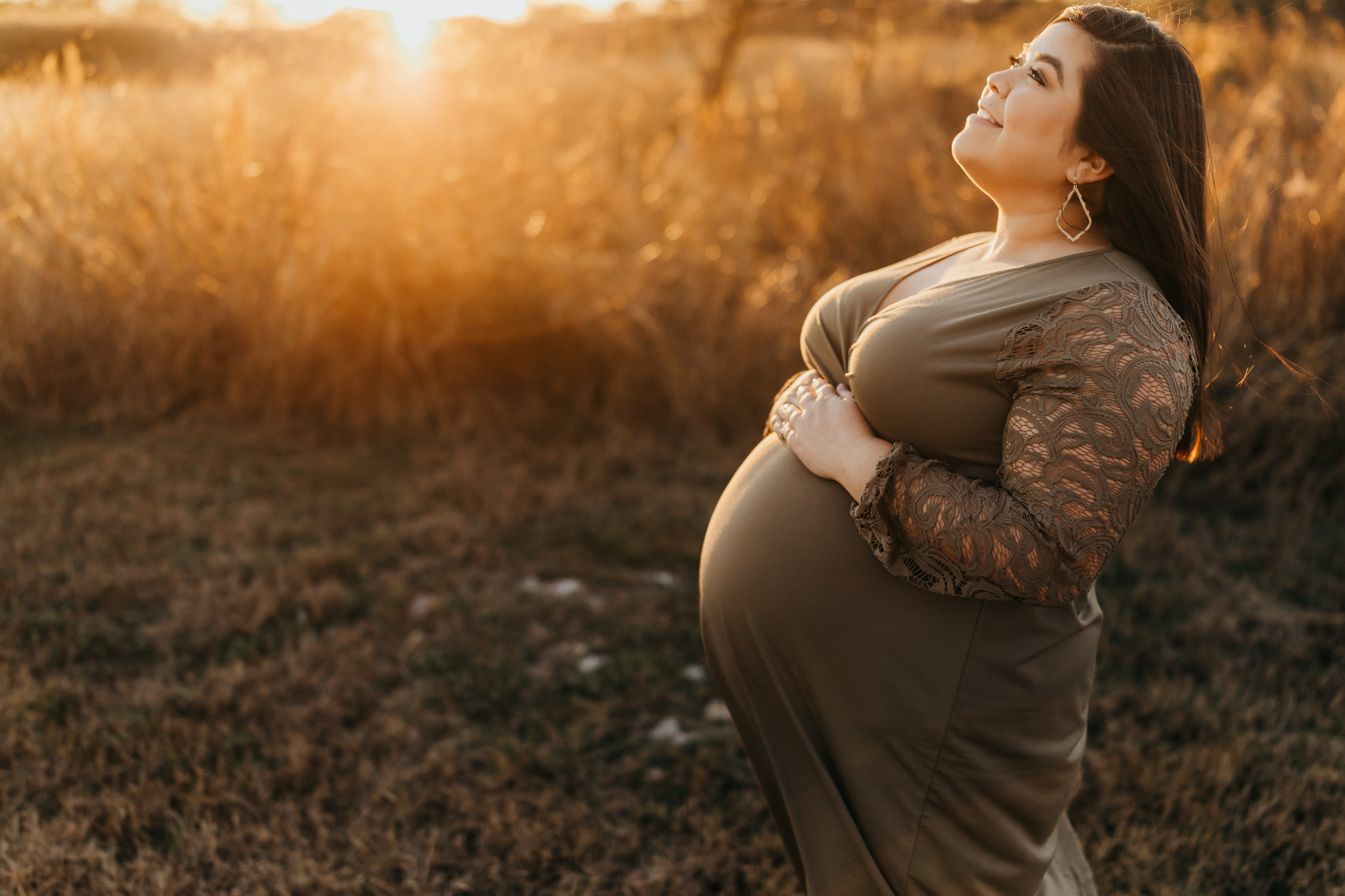pregnant mama holding her belly in a field, during golden hour, wearing an olive dress.