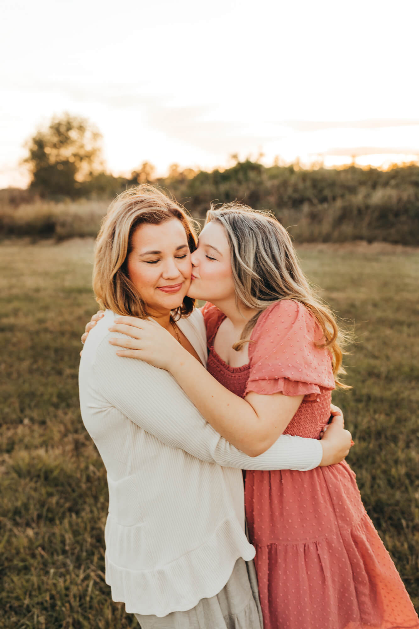 Teen daughter kisses mom on the cheek while mom embraces the love from her after going to Mother's day brunch in houston.