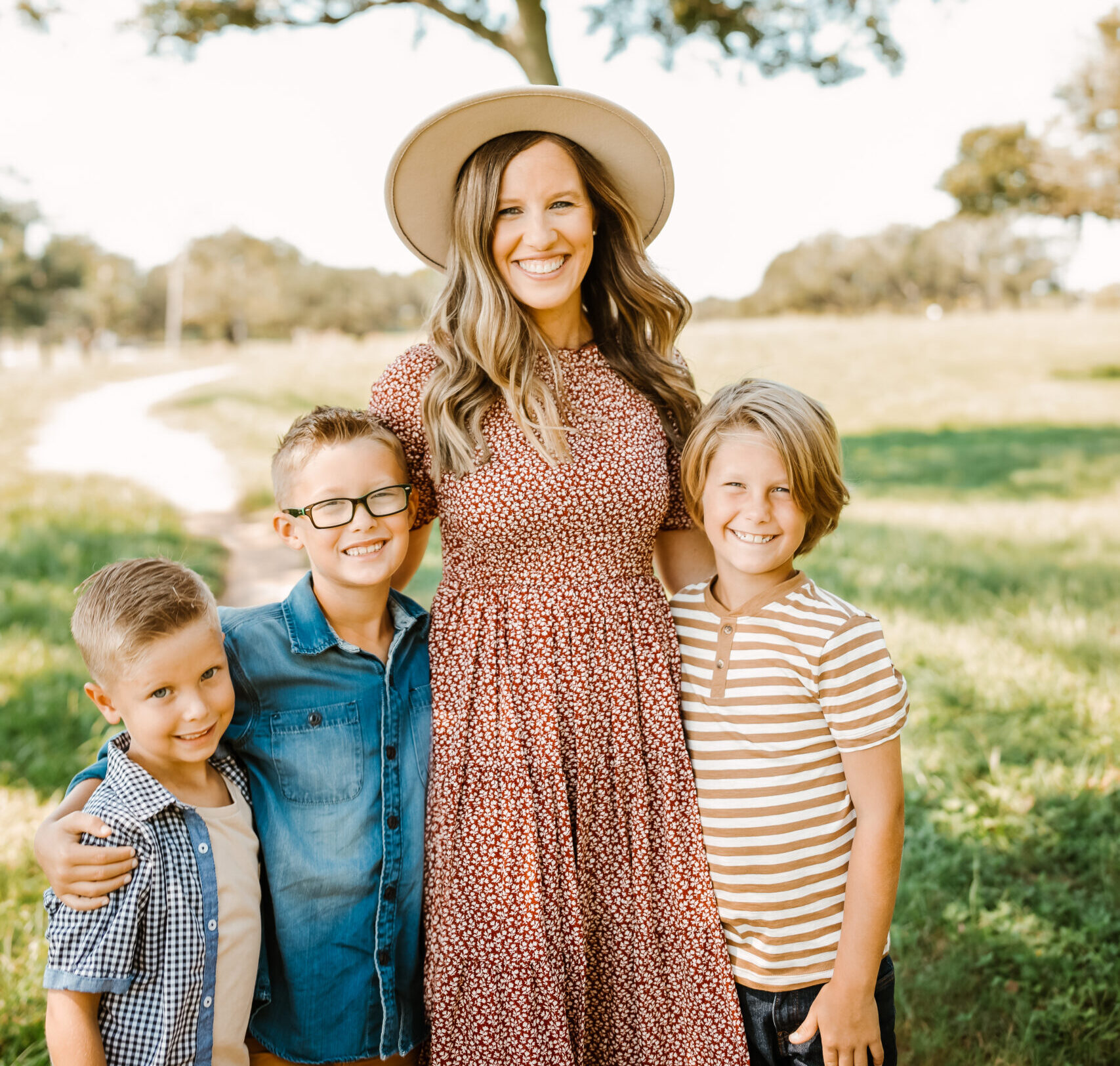 Mom with her sons, standing in the park for photographs with Ally's Photography. Mom is stylish and wearing a hat, and kids are dressed in nice clothes, purchased at Just Between Friends Pearland