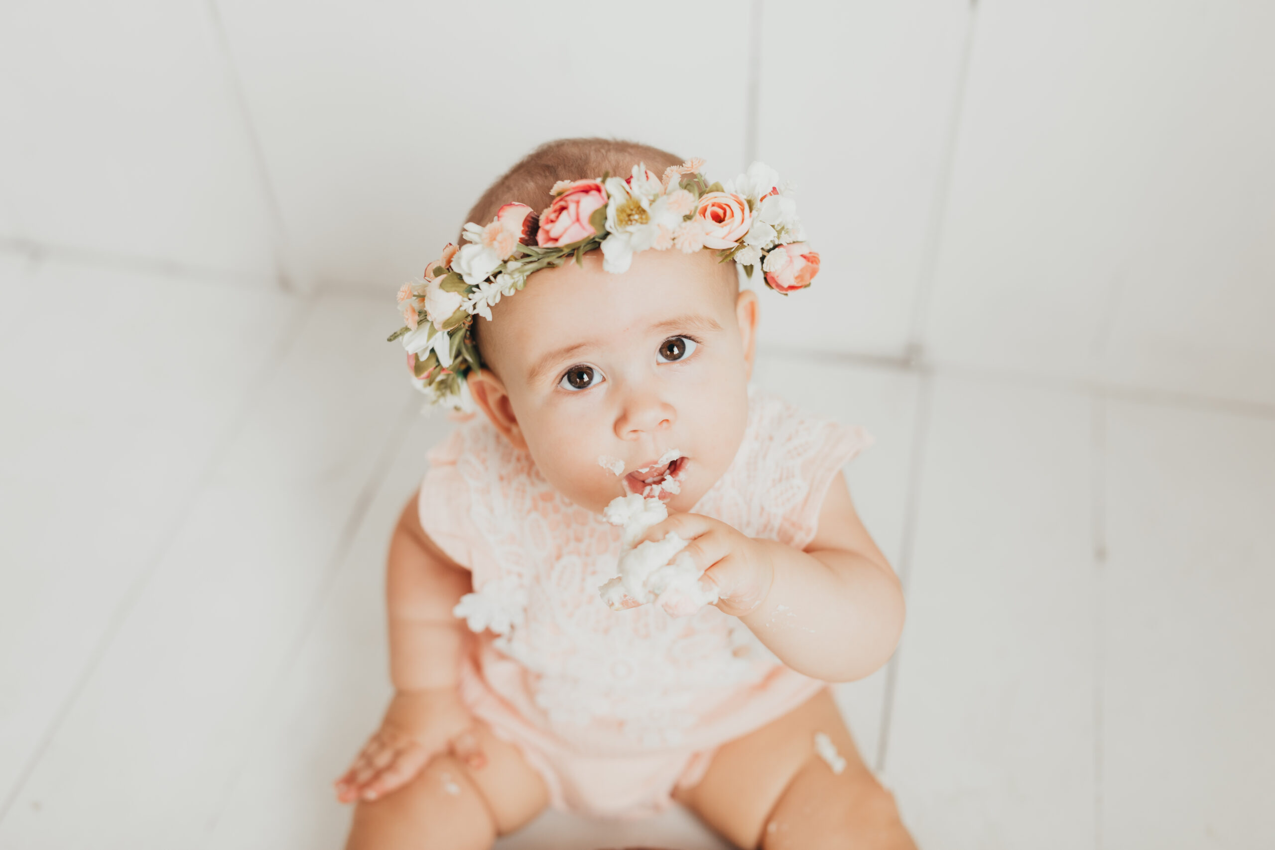 Baby looks up at camera while licking icing off her fingers from her houston cake smash photography session.