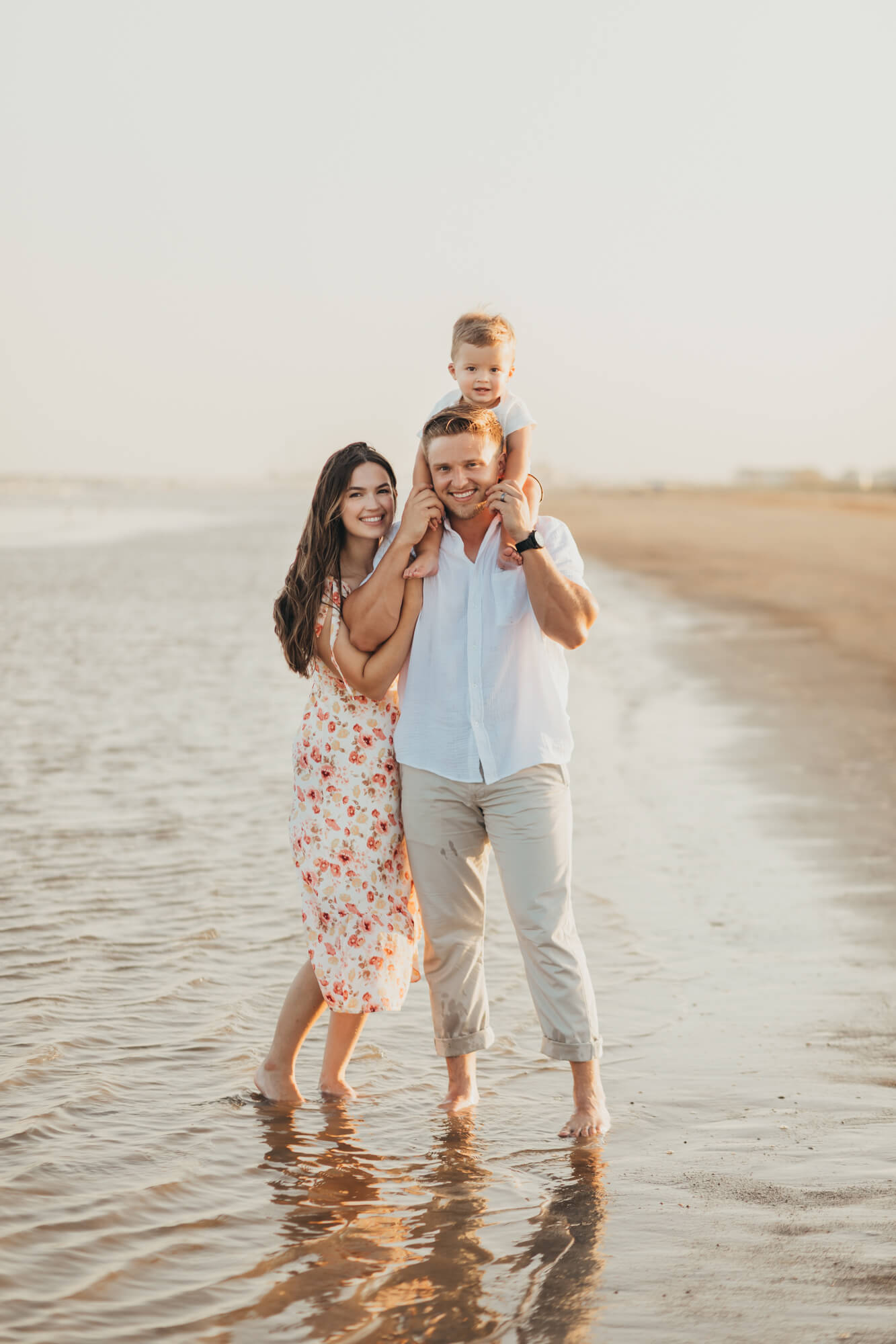 mom and dad hold baby toddler on the beach in Galveston Texas with ally's photography
